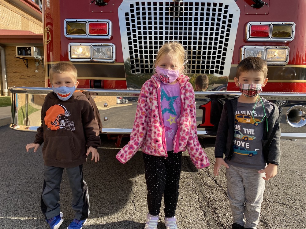 Three preschool students in front of a fire truck